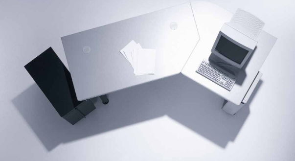 1982 Schreibtisch-Design Ein moderner Bürotisch mit einem Computer und Papieren in einem minimalistischen weißen Umfeld.