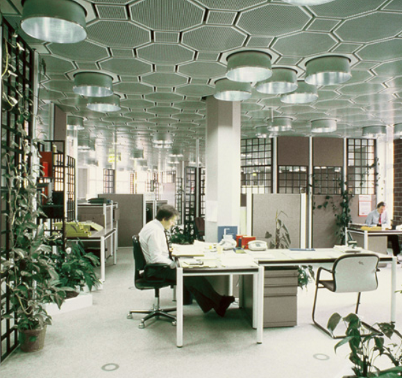 70er Büro-Design Moderne Büroeinrichtung mit einzigartigen sechseckigen Deckenmustern, Pflanzen und Arbeitern an den Schreibtischen.